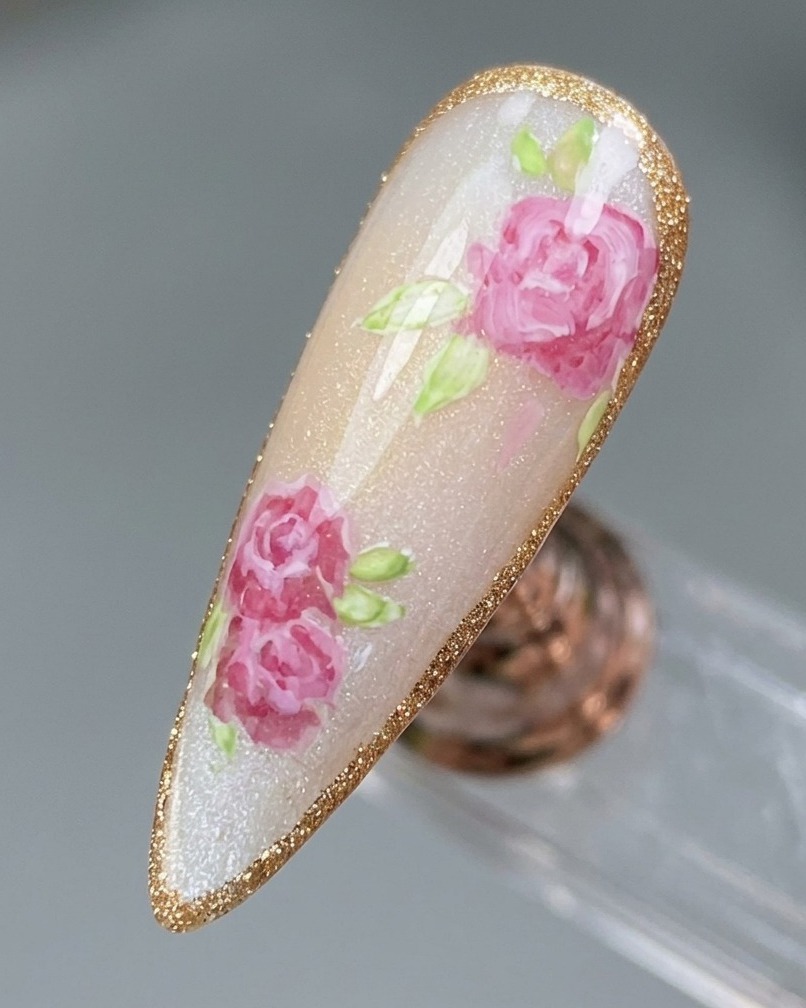 Primer plano de un diseño de rosa finalizado siendo delineado con un borde de gel platino brillante.