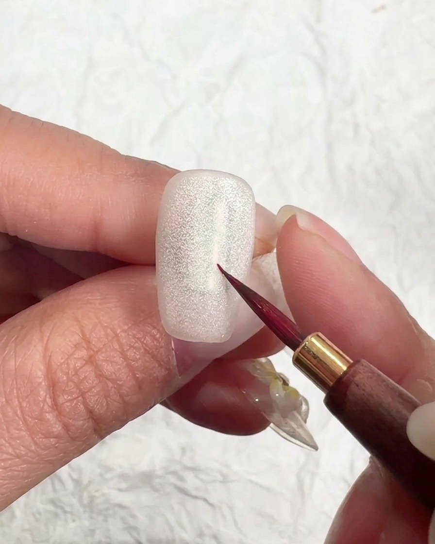 Pincel aplicando una capa suave de gel top coat mate sobre una uña brillante ojo de gato.