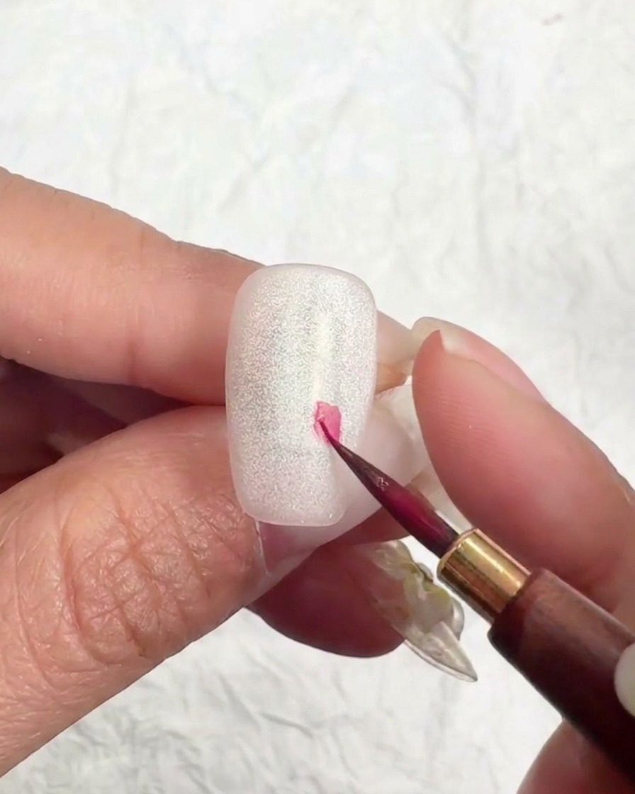 Pincel liner fino colocando un pequeño punto rosa en la uña para iniciar la flor de cerezo.