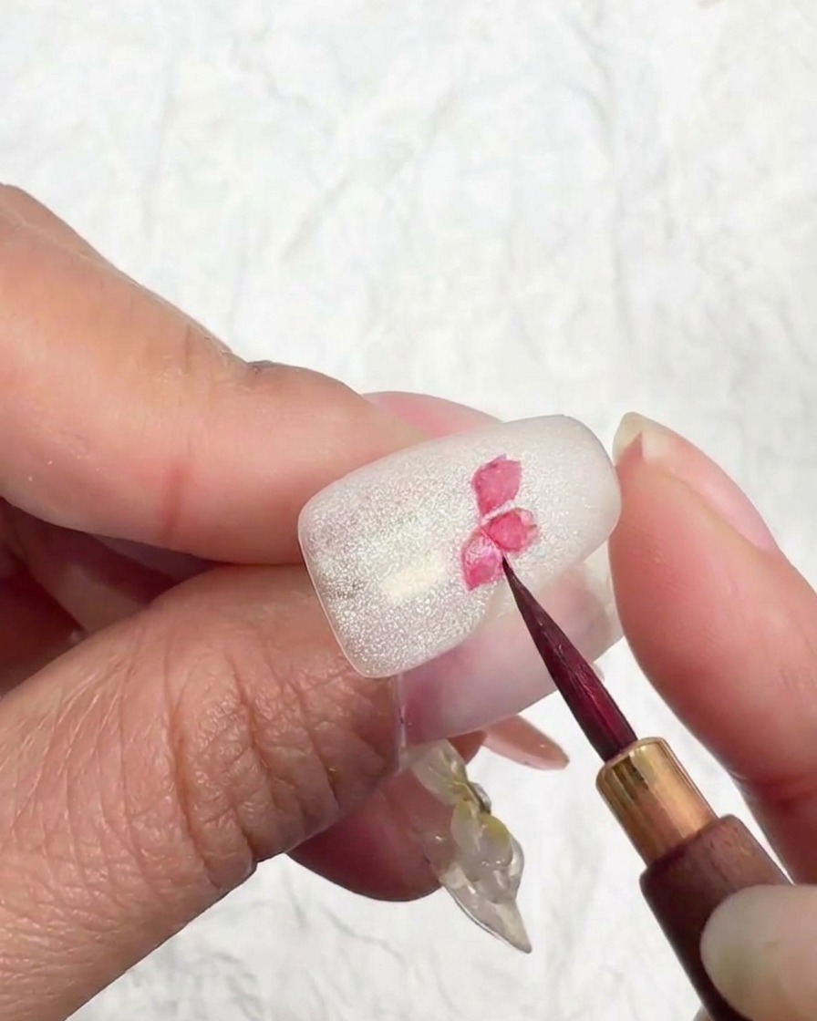Primer plano de un diseño de flor de cerezo en una uña, añadiendo pigmento rosa más claro a las puntas de los pétalos.
