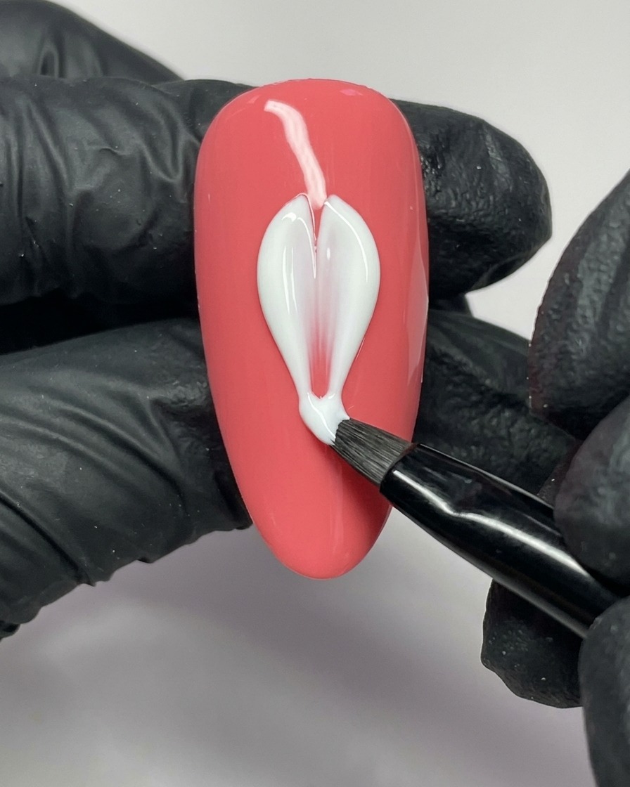 Un pincel de arte de uñas aplicando gel blanco para formar el lado izquierdo de un pétalo en una uña rosa.