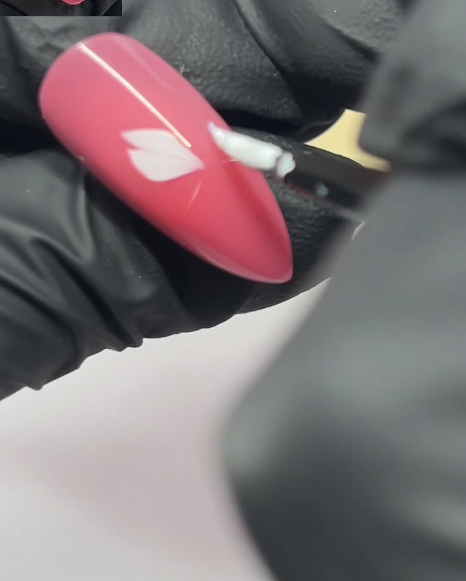 Un pincel de arte de uñas aplicando un segundo pétalo junto al primero en una uña rosa.