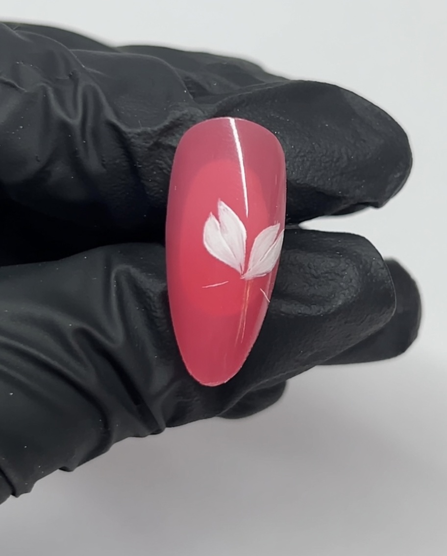 Primer plano de una uña que muestra tres pétalos blancos de un diseño de flor de cerezo sobre una base rosa.