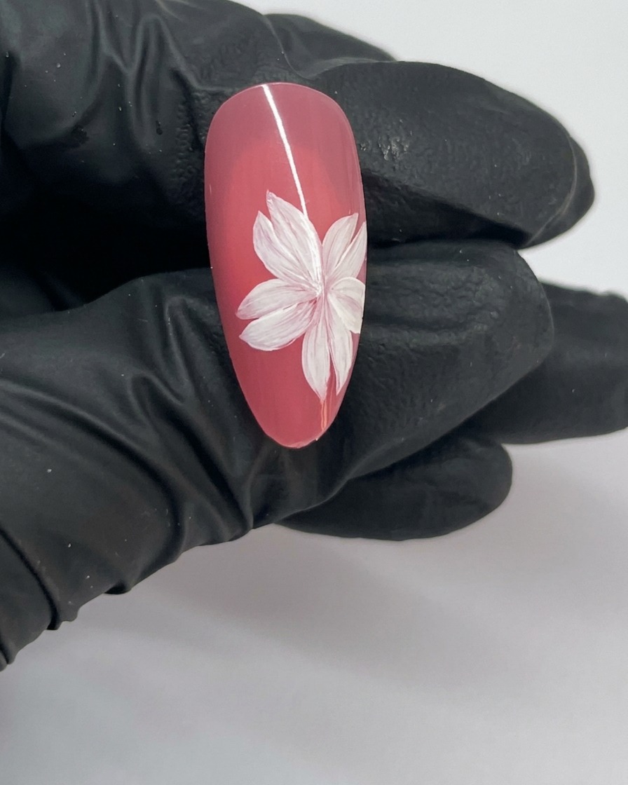 Primer plano de un diseño de arte de uñas de flor de cerezo terminado, con una flor completa y un estambre blanco en el centro.