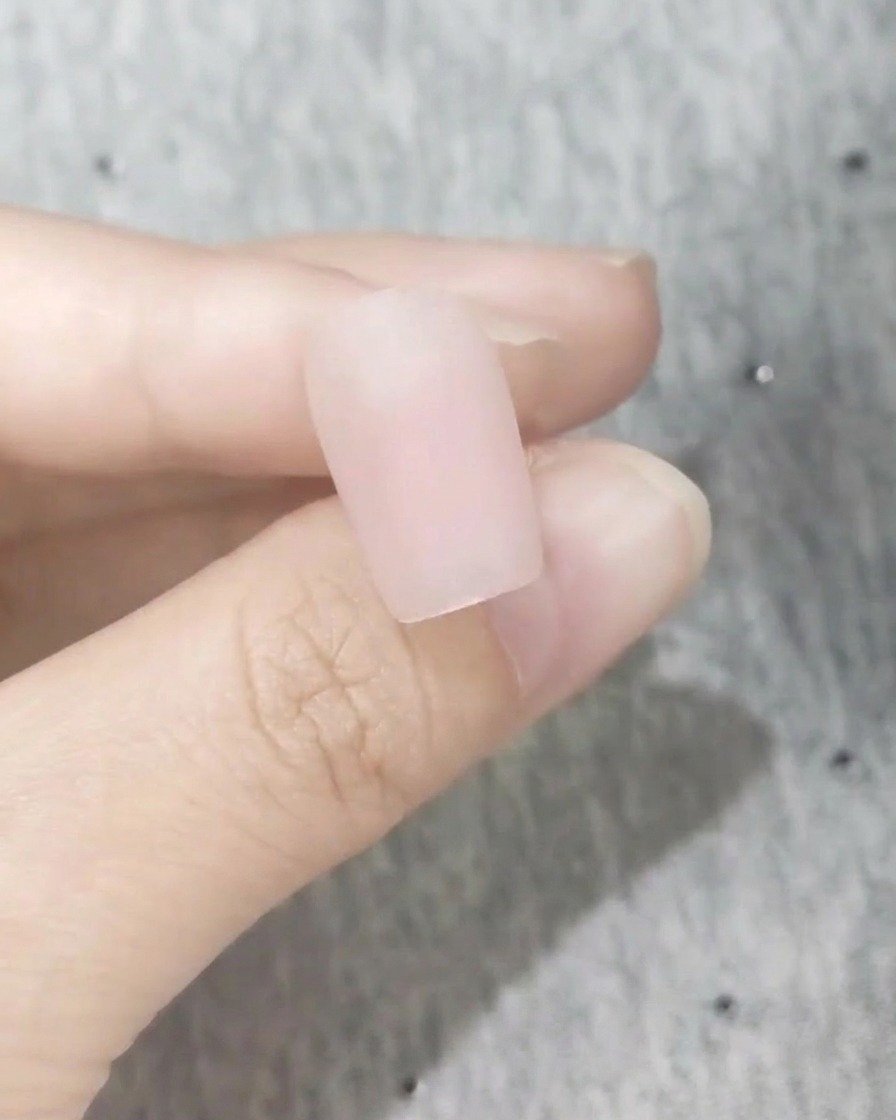 Primer plano de una uña con un acabado impecable de esmalte rosa mate.