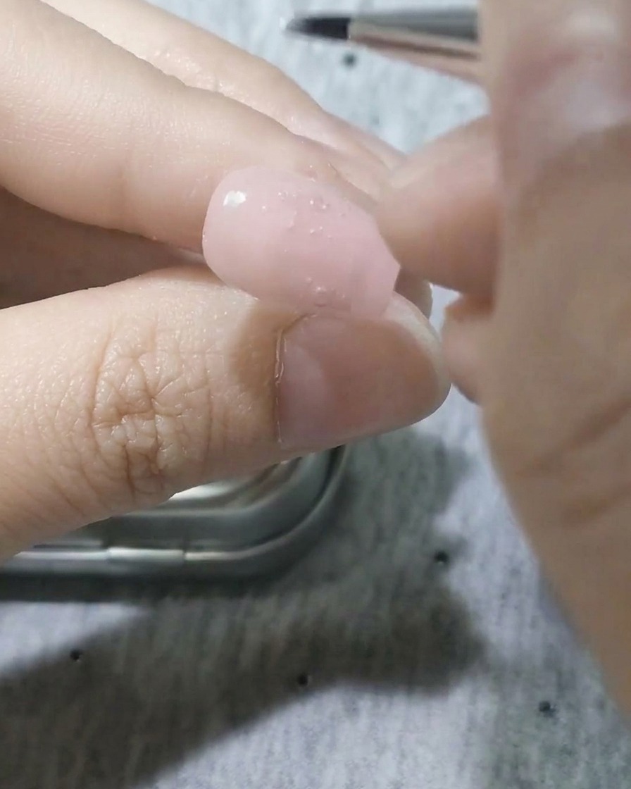 Un pincel de detalle fino aplicando gel blanco para formar la figura de un pétalo.