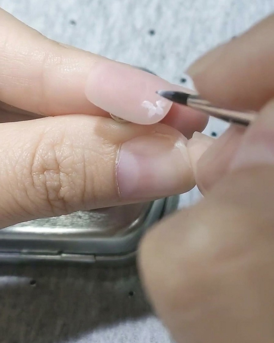 Primer plano de un pincel de detalle pintando pétalos blancos semitransparentes sobre una base rosa mate.