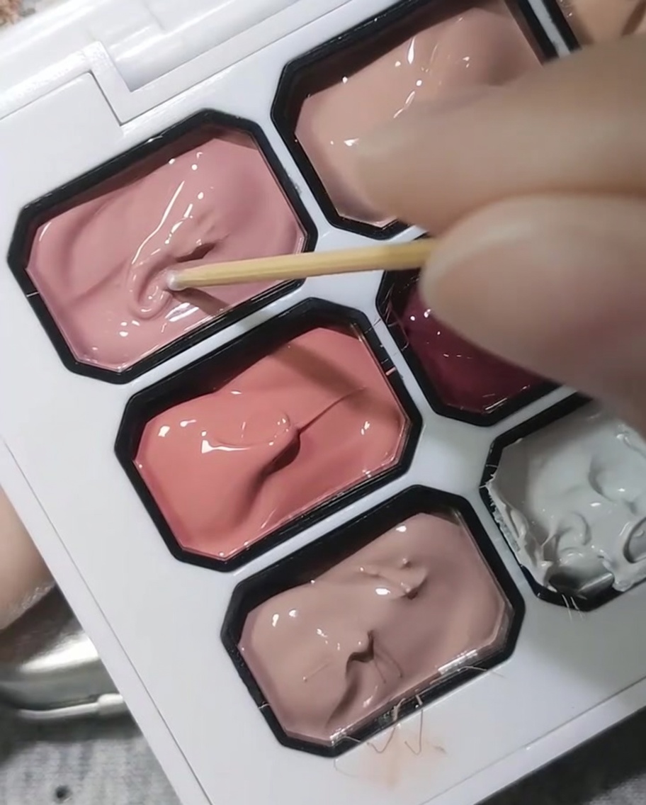 El extremo de un palillo de madera sumergiéndose en una paleta de gel rosa opaco.