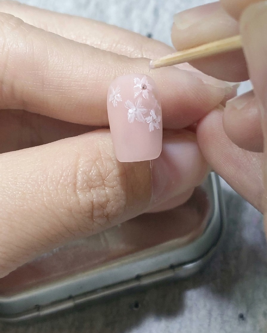 Un palillo colocando puntos de gel rosa oscuro en el centro de las flores blancas sobre una uña rosa.