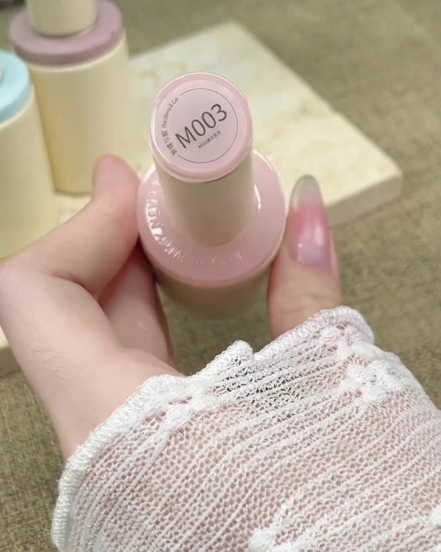Pincel de uñas aplicando un esmalte en gel rosa nude traslúcido sobre una extensión de uña.