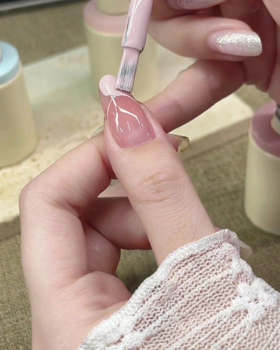 Un pincel de uñas rellenando el área de la punta francesa con esmalte en gel rosa pastel.