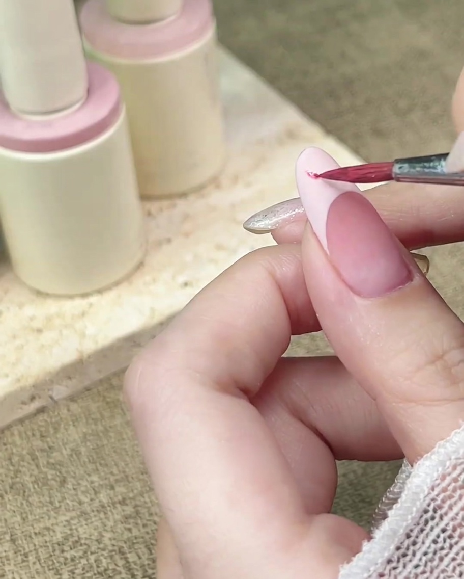 Un pincel de detalle aplicando acuarela rosa sobre una punta francesa con acabado mate.