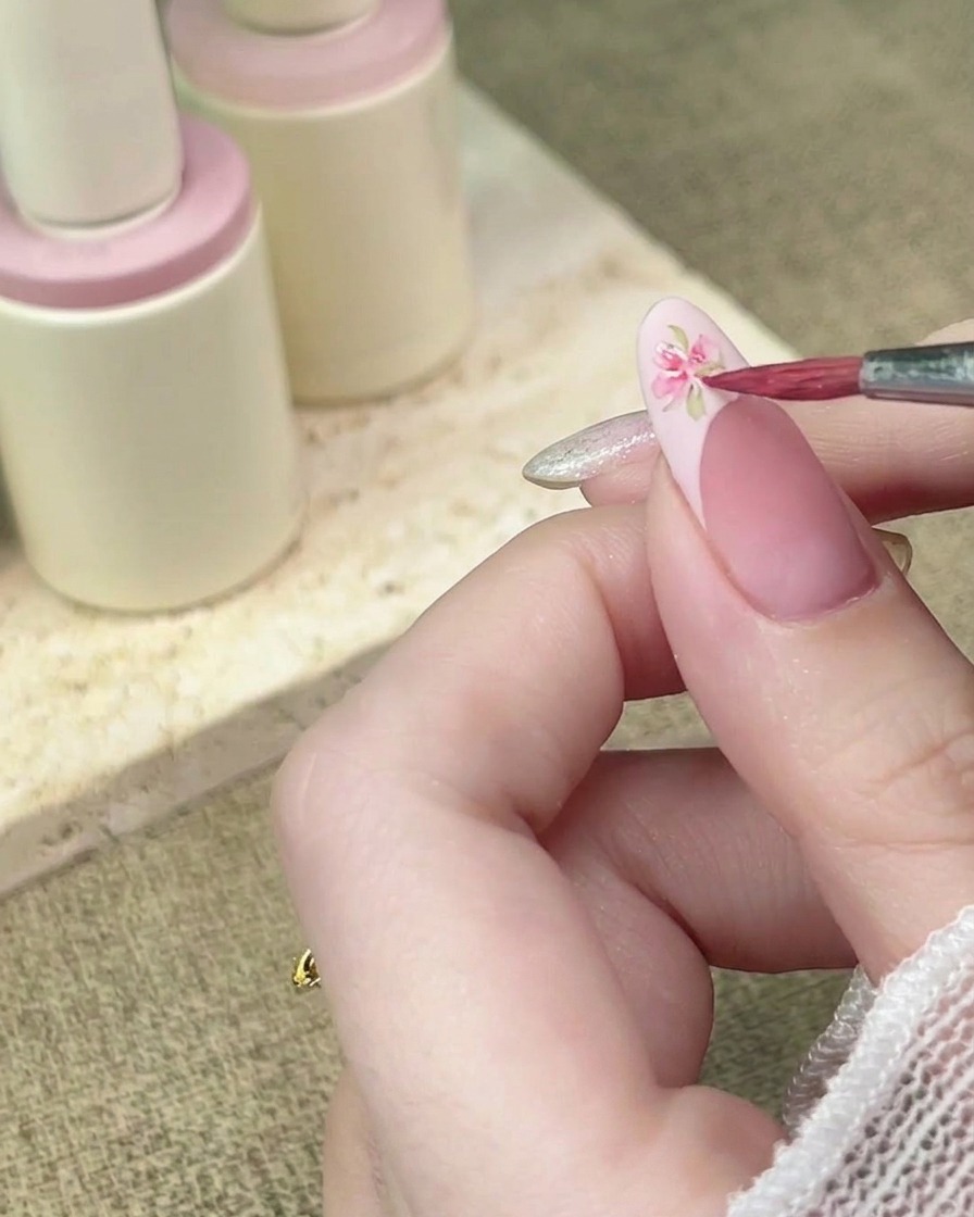 Un pincel de detalle agregando más pétalos de acuarela rosa para completar un diseño floral en una punta francesa.