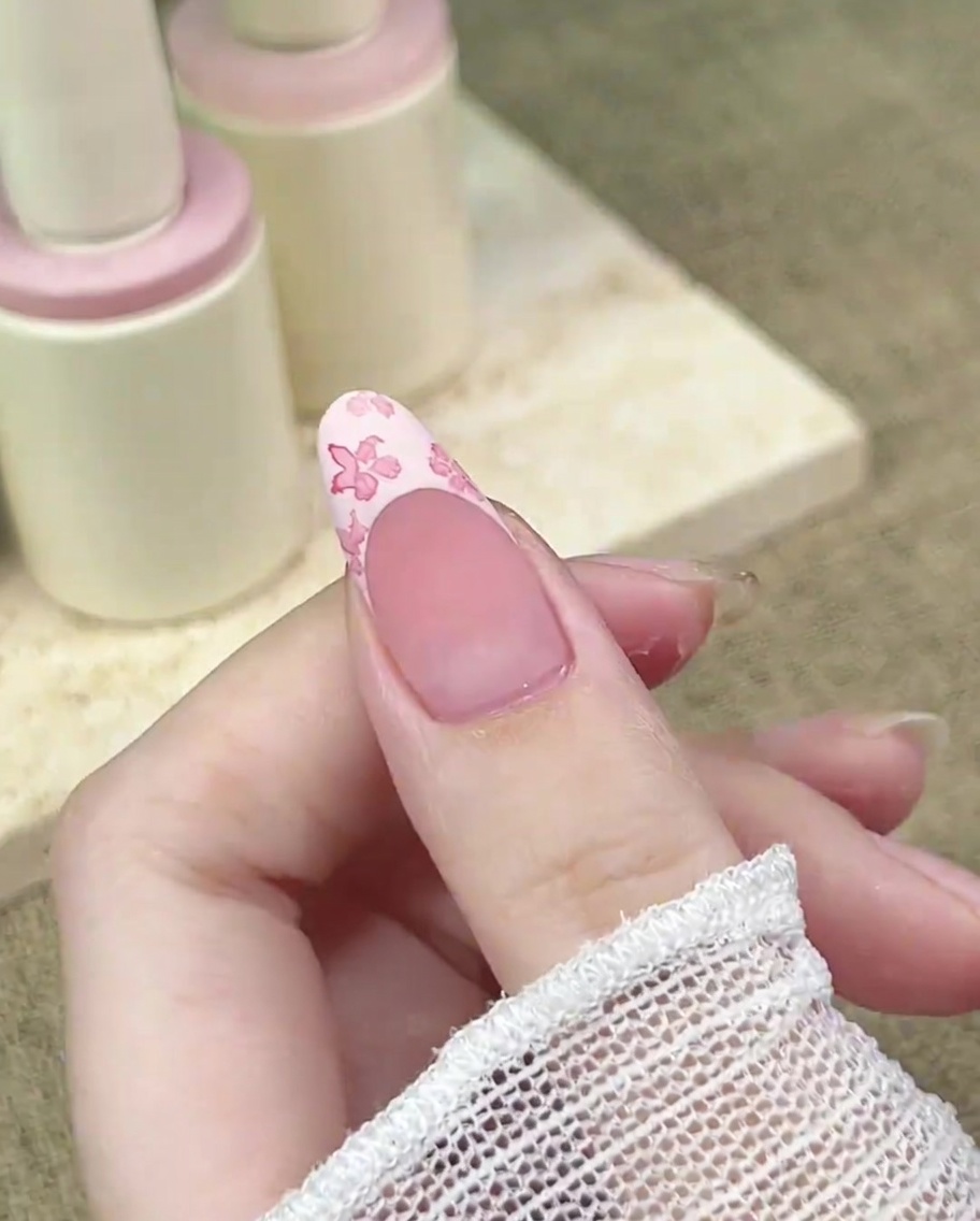 Primer plano de un pincel de detalle agregando un punto concentrado de rosa oscuro al centro de un diseño floral en una uña.