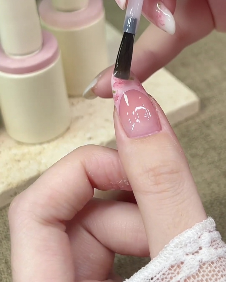 Un pequeño dije de lazo rosa 3D siendo colocado en el centro de la línea de sonrisa francesa usando una herramienta de puntos o pinzas.