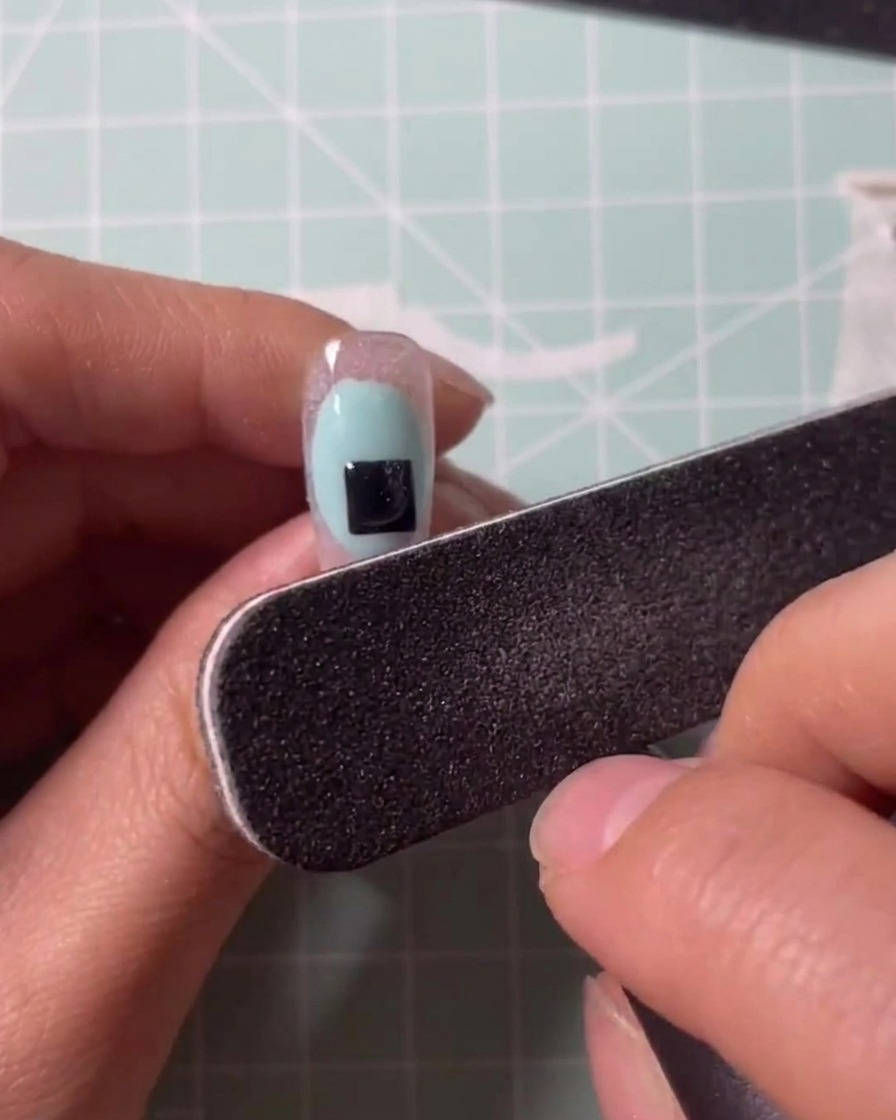 Un pincel aplicando gel transparente sobre un tip de extensión.