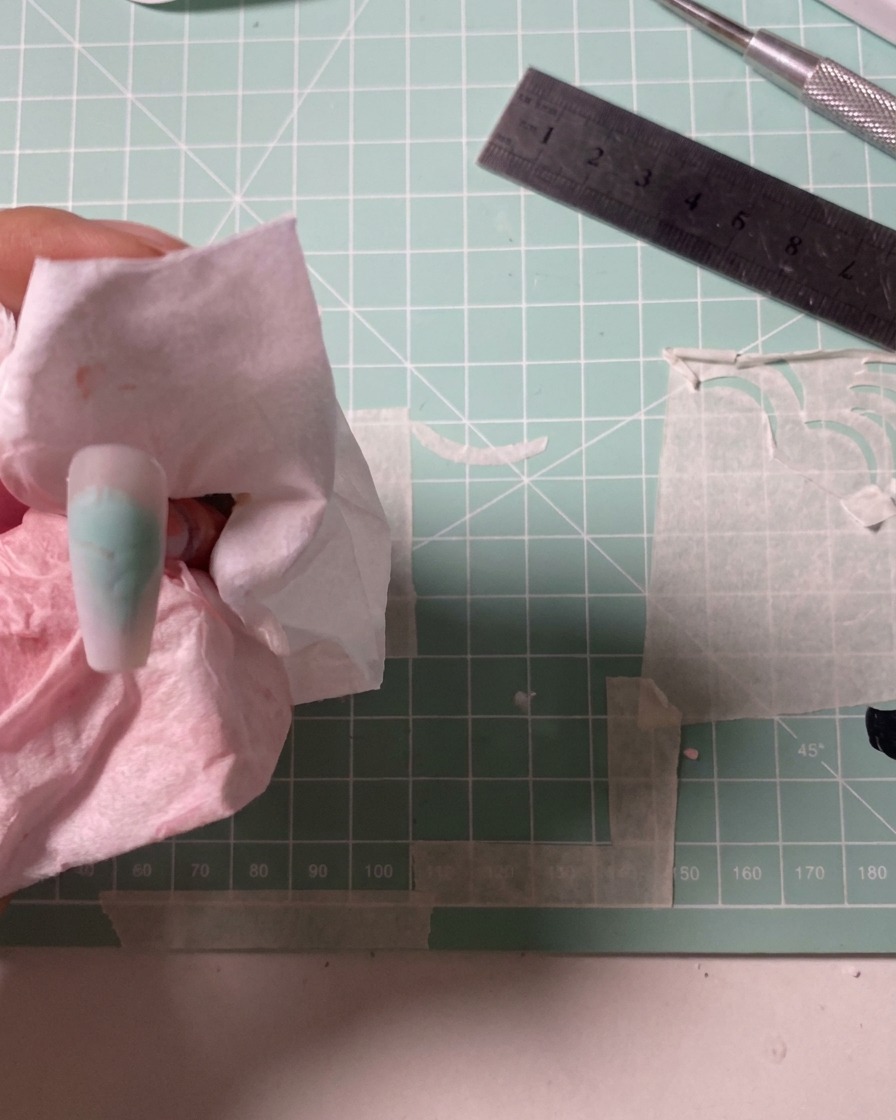 Un aerógrafo siendo utilizado para aplicar un color rosa empolvado suave sobre una uña.