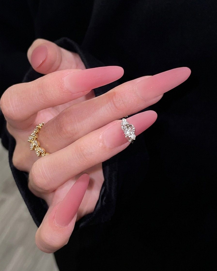Una mano con uñas largas degradadas en rosa posada elegantemente sobre un fondo de manga negra, resaltando la transición de un nude transparente a un rosa oscuro.