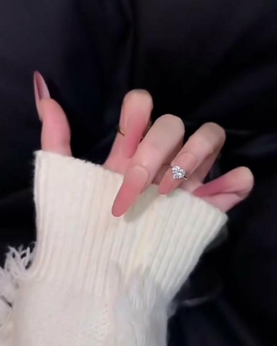 Primer plano de uñas largas cónicas en degradado rosa sobre fondo negro, mostrando un acabado suave y aterciopelado difuminado.