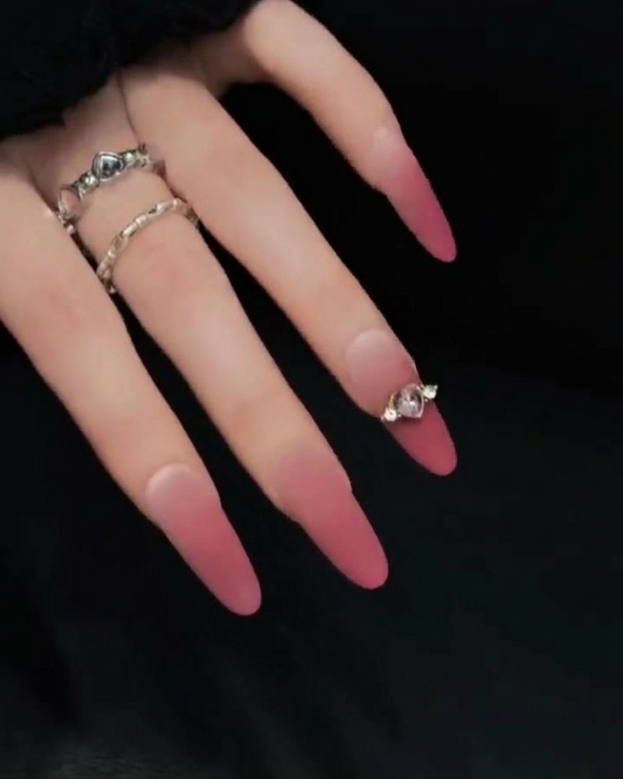 Primer plano de una mano posada contra un fondo oscuro, mostrando el perfil lateral de uñas press-on degradadas en rosa y nude para resaltar su longitud y curvatura.