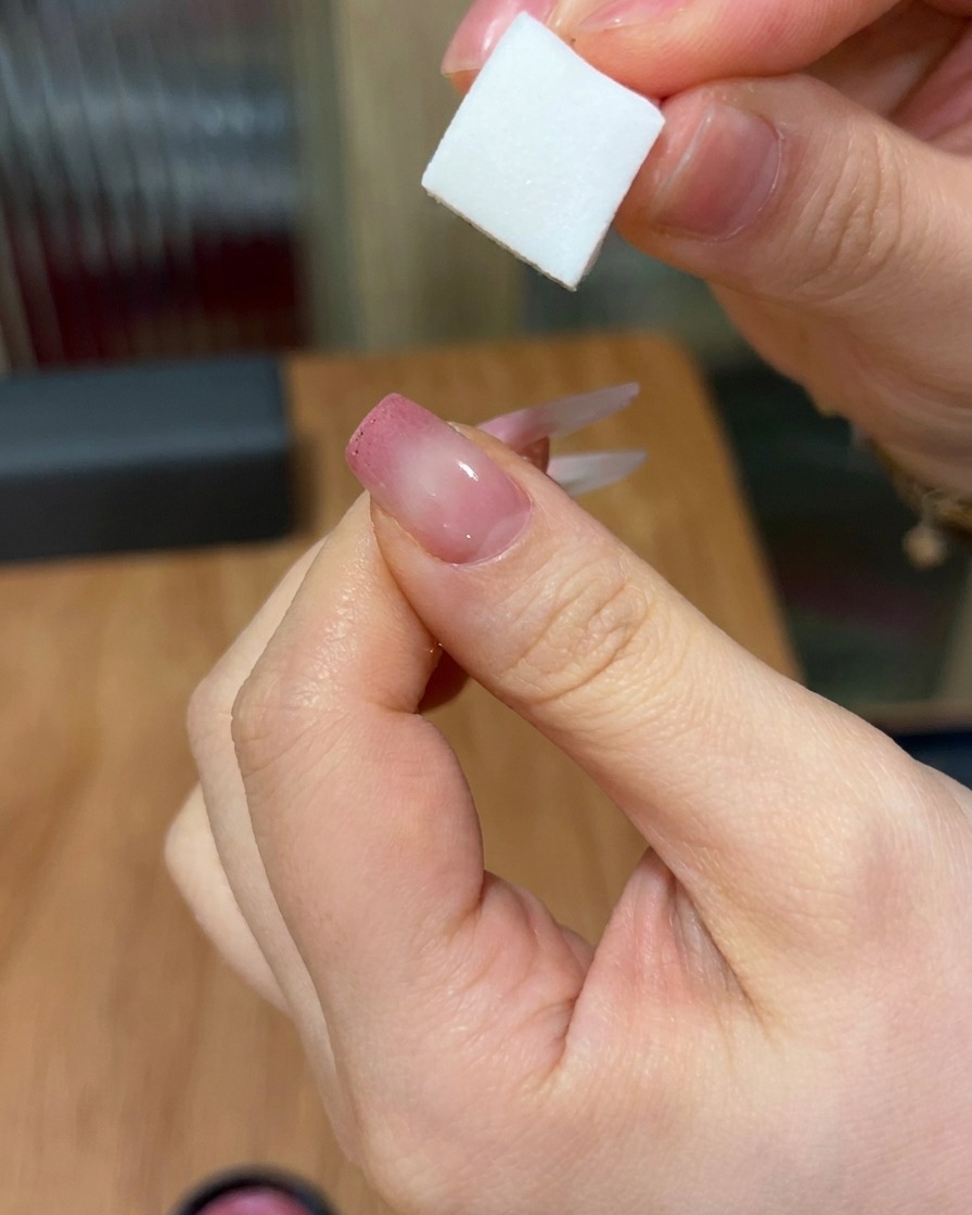 Primer plano mostrando una esponja aplicando gel rosa sobre una uña, creando un degradado suave y difuminado desde la punta hacia el centro.