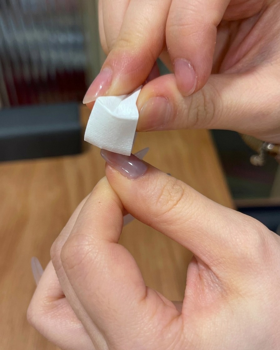 Primer plano de una cuña de esponja blanca siendo utilizada para dar toques de gel rosa sobre la punta de una uña.