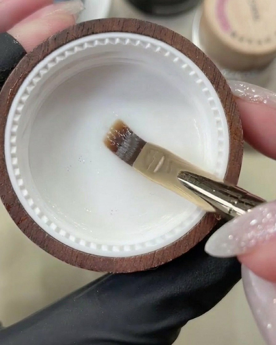 Un pincel de gel aplicando una capa base transparente sobre una uña natural limpia.