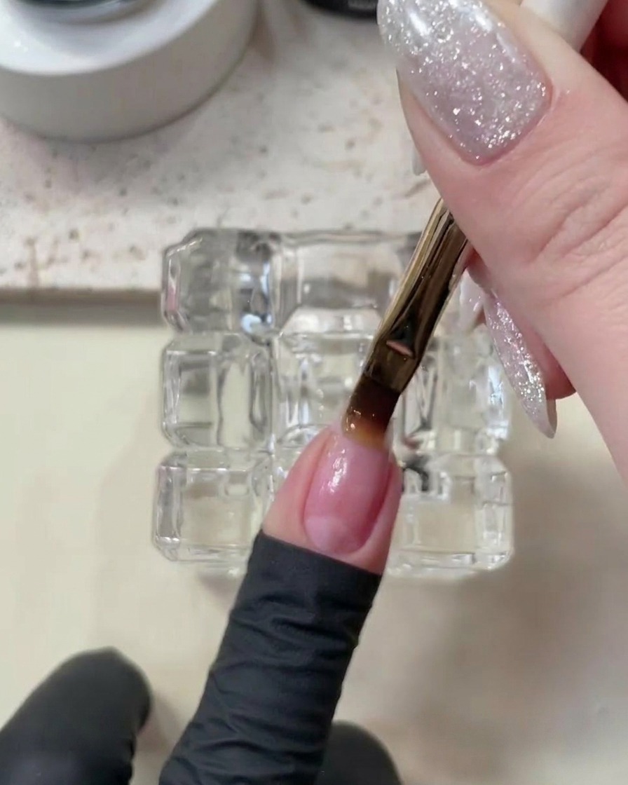 Una mano dentro de una lámpara UV/LED curando la capa base de las uñas.