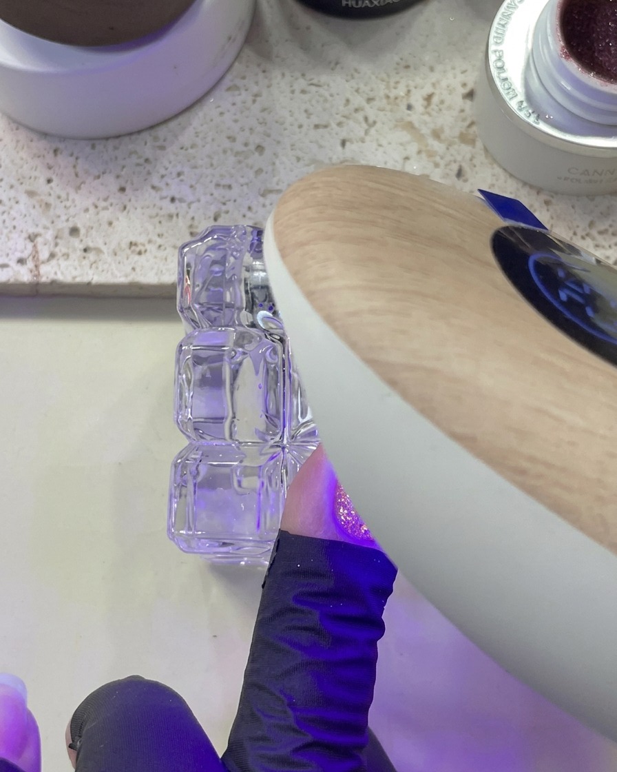 Una mano bajo una lámpara UV/LED curando el glitter aplicado sobre las uñas.