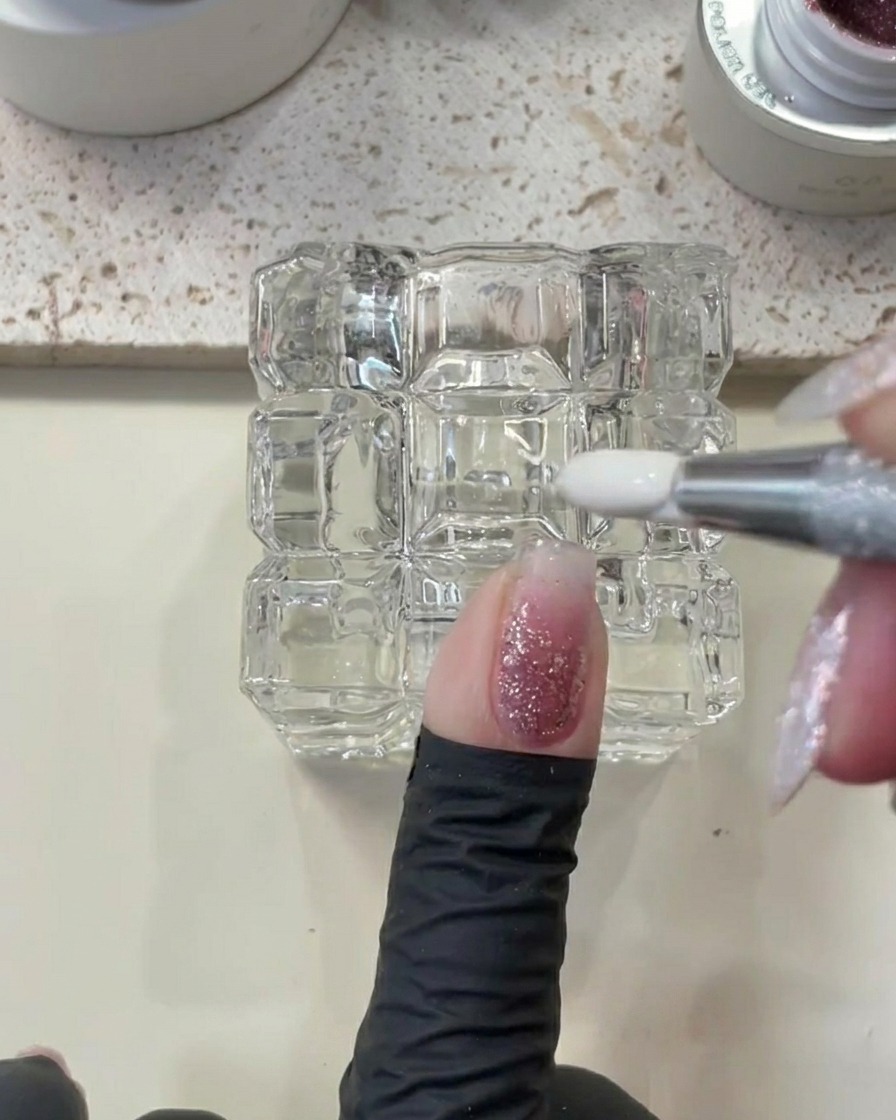 Una herramienta metálica limpiando el exceso de gel cerca de la cutícula.