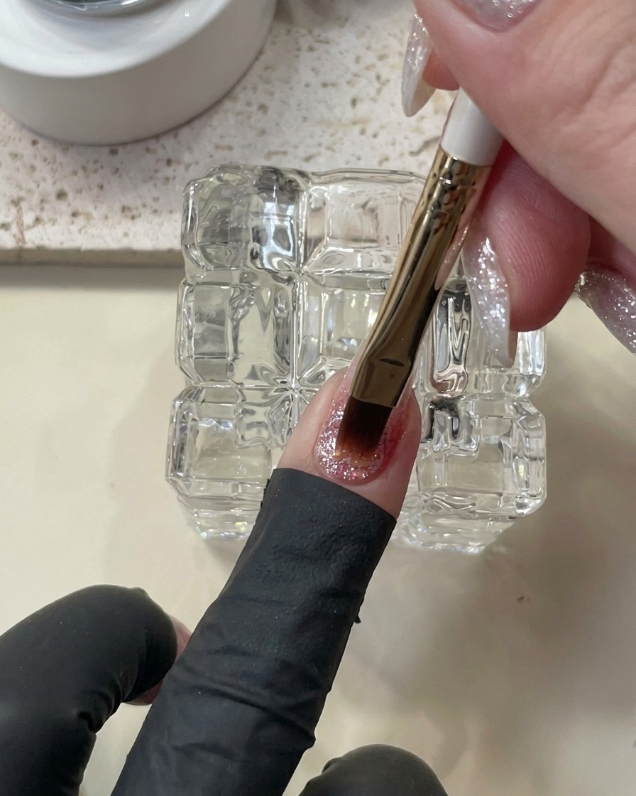 Un pincel aplicando una gota niveladora de builder gel para dar estructura a la uña.