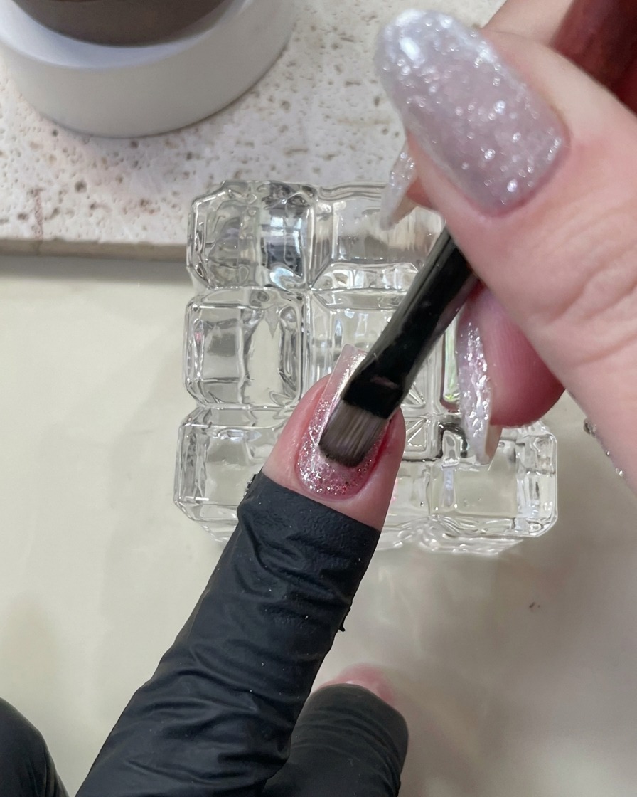 Un pincel aplicando esmalte nude de efecto cat eye sobre la capa de builder gel.