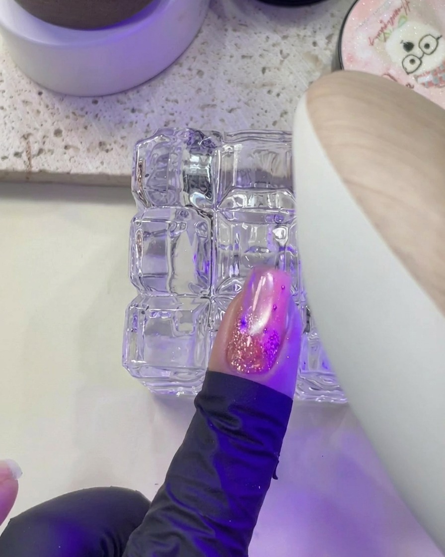 Una mano colocando las uñas bajo la luz púrpura de una lámpara UV/LED.