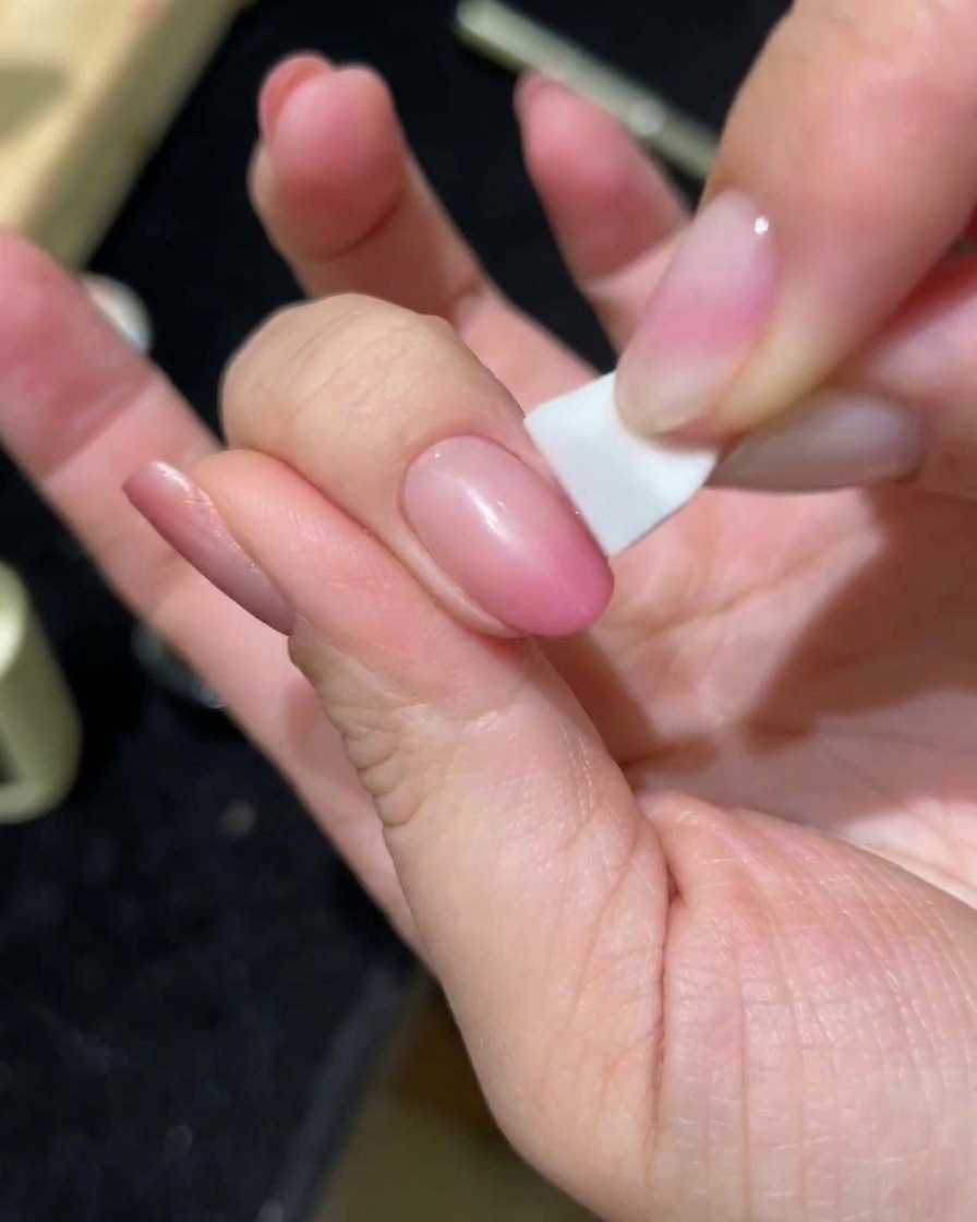 Una mano aplicando una segunda capa de gel cat-eye rosa sobre la uña usando una esponja.