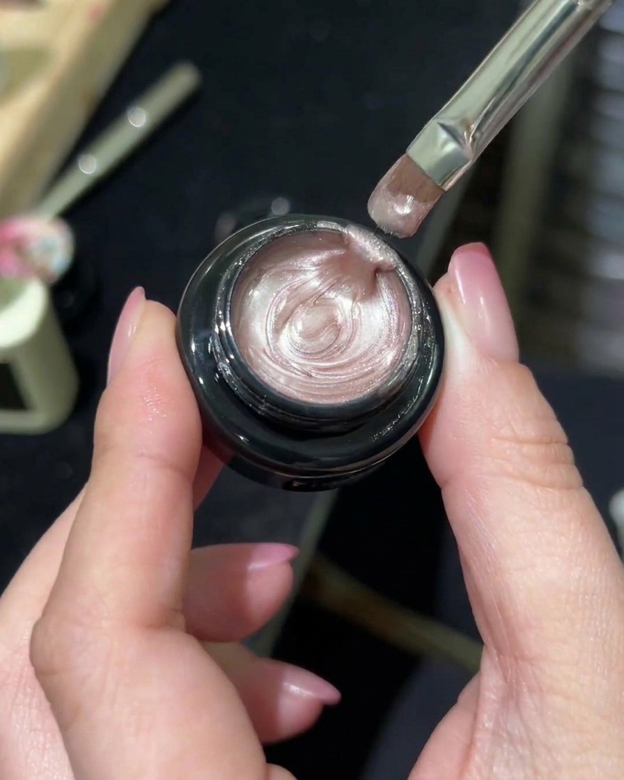 Un pincel profesional de manicura tomando gel magnético con efecto aurora desde un tarro.