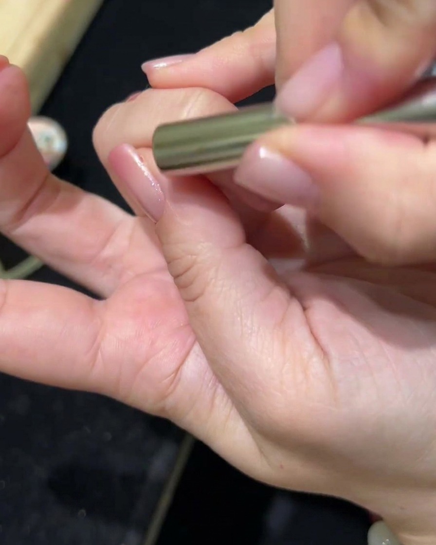 Una varita magnética sobre una uña recubierta de gel, mostrando el pigmento desplazándose para crear el efecto magnético.