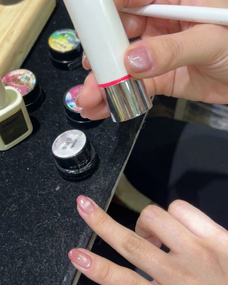 Una mano descansando dentro de una lámpara LED para uñas encendida, curando las uñas con gel cat-eye.