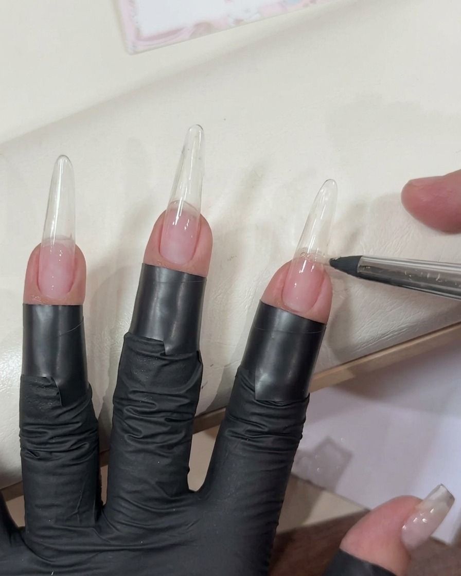 Aplicando un gel rosa claro traslúcido sobre una extensión de uña transparente con un pincel plano.
