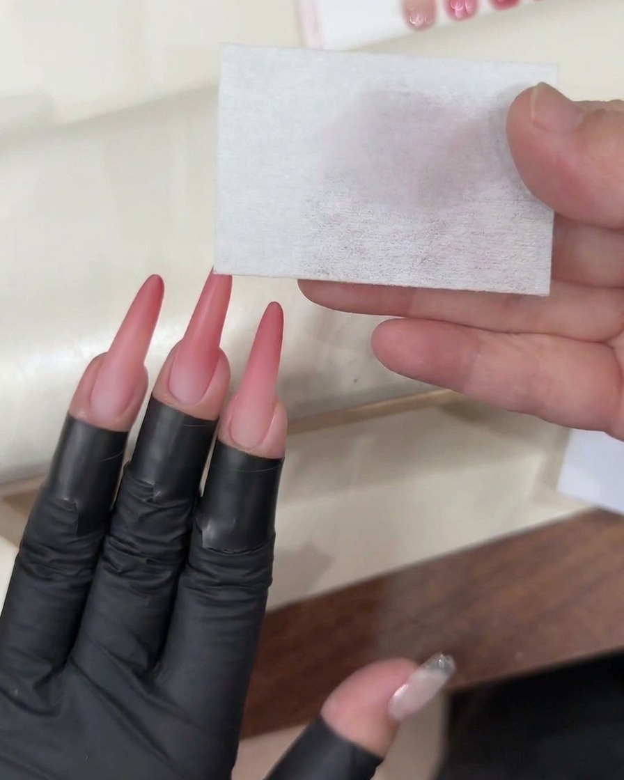Un pincel de gel aplicando una capa final transparente y brillante sobre la uña ombré rosa terminada.