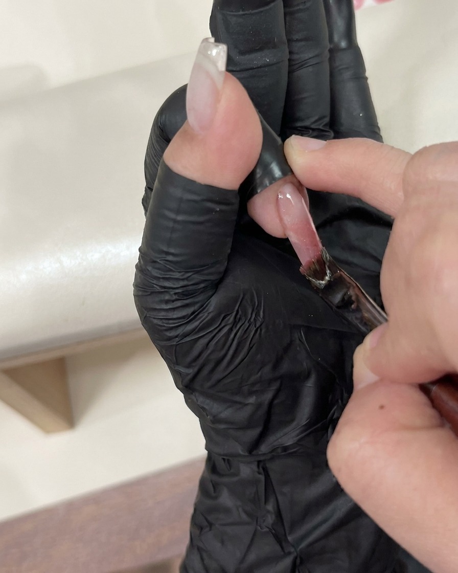 Un par de pinzas colocando cuidadosamente un pequeño dije decorativo sobre una uña con top coat húmedo.
