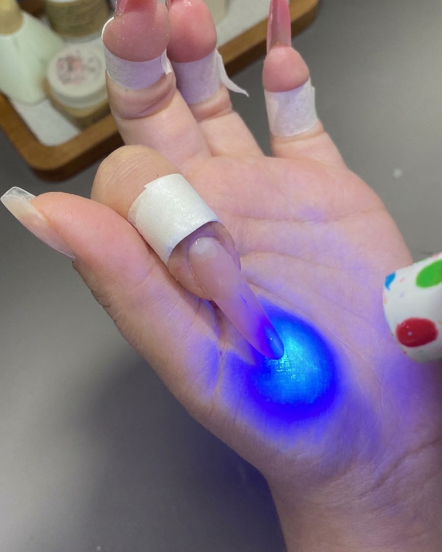 Una mini lámpara UV/LED de mano que emite una luz azul para curar el gel en una uña.