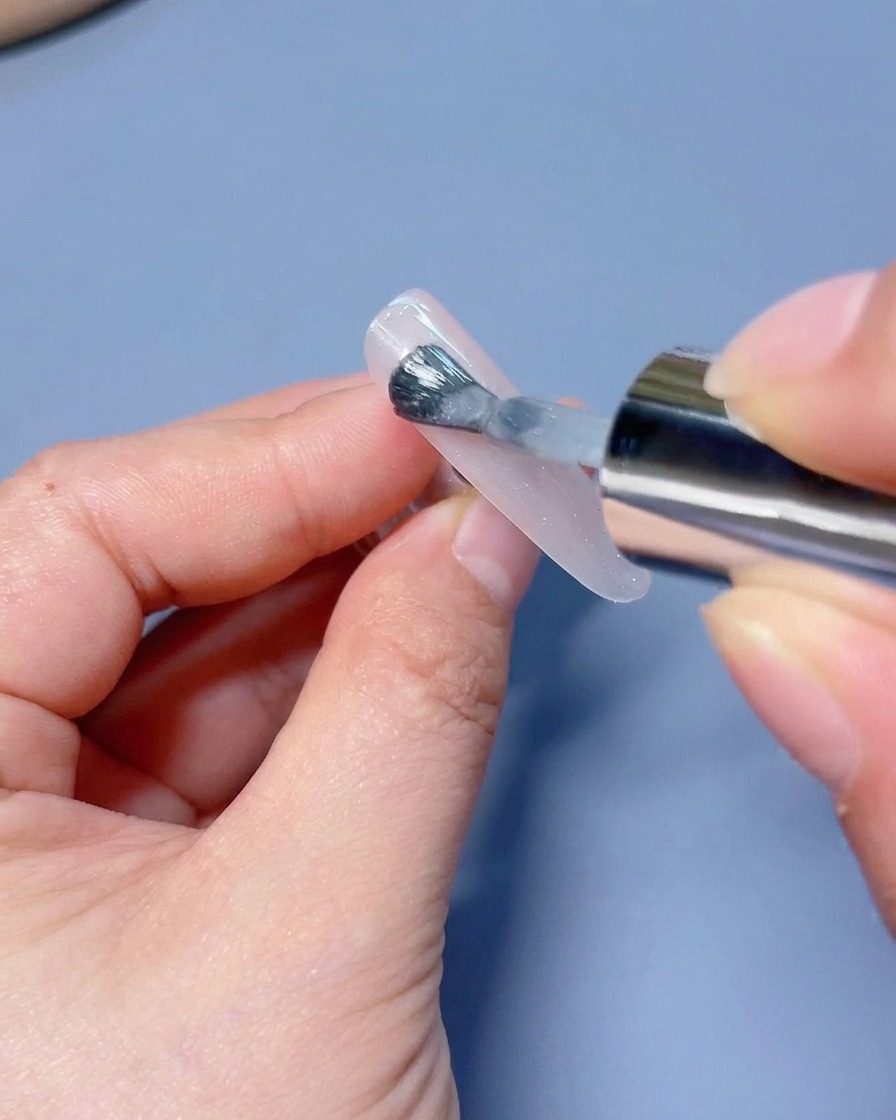 Un pincel aplicando una capa de esmalte de gel ojo de gato blanco brillante sobre un tip de uña.