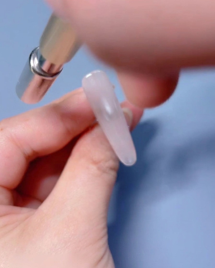 Una herramienta magnética colocada cerca de la uña con gel húmedo para manipular las partículas de brillo.
