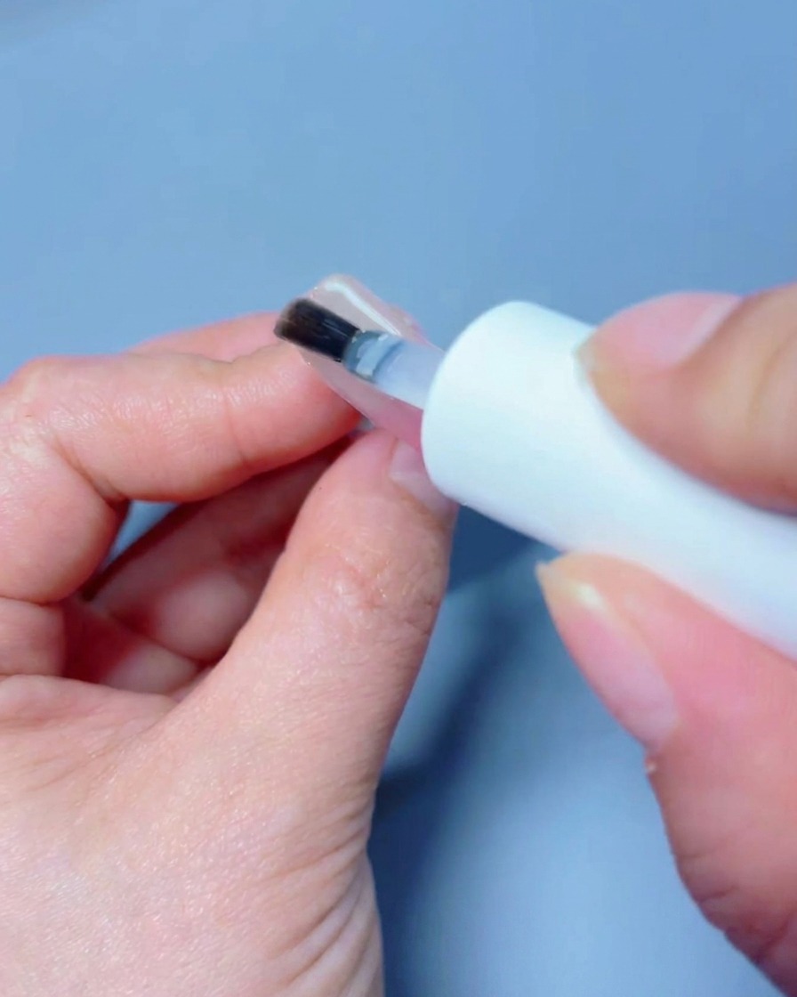 Una mano posicionada bajo una lámpara UV/LED profesional curando la capa final de top coat.