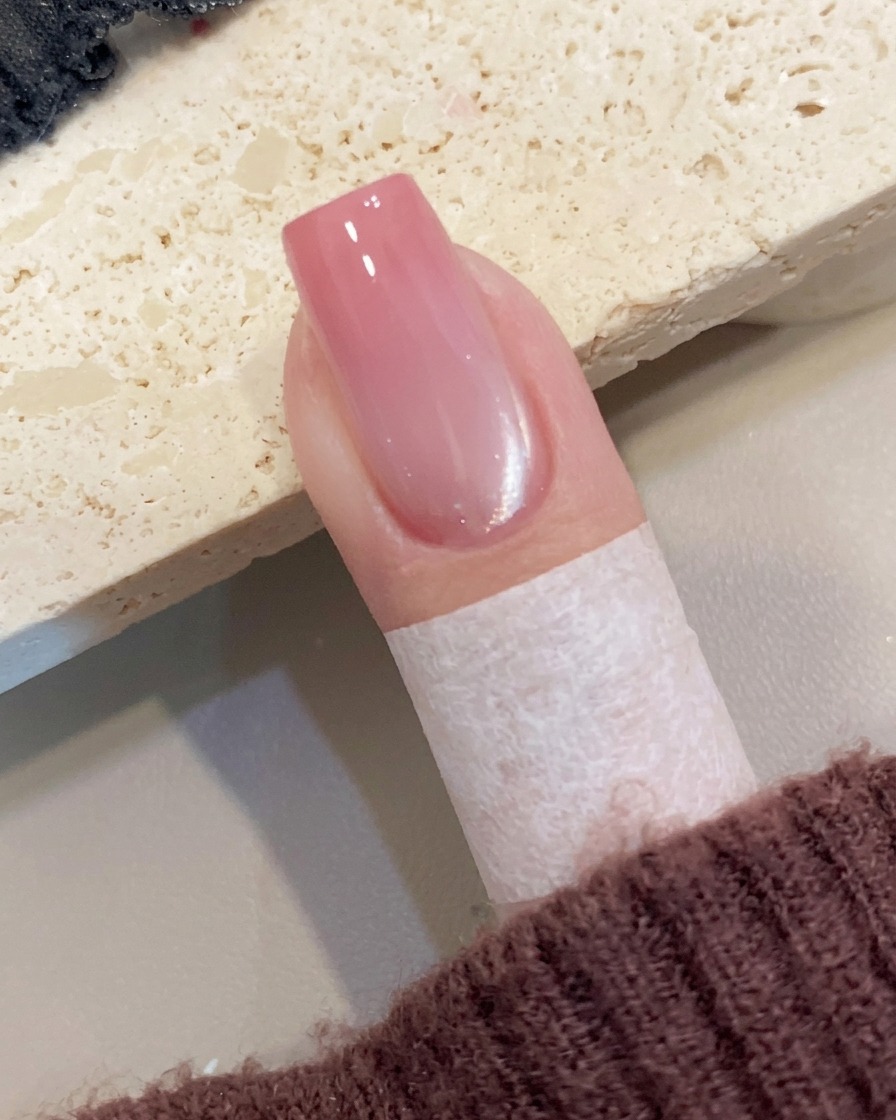 Primer plano de una mano retirando cuidadosamente la cinta protectora de la piel que rodea la uña.