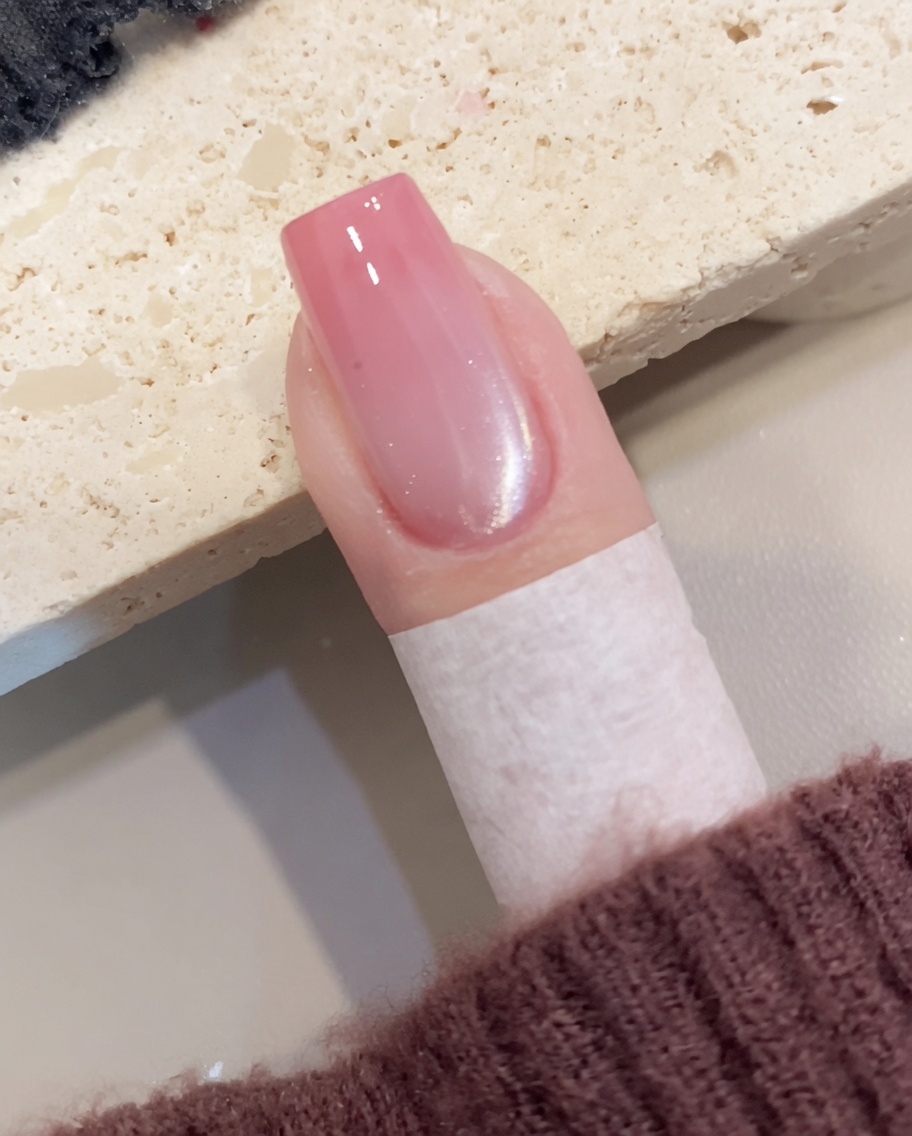 Primer plano mostrando un pincel aplicando esmalte en gel cat-eye brillante sobre una uña preparada.