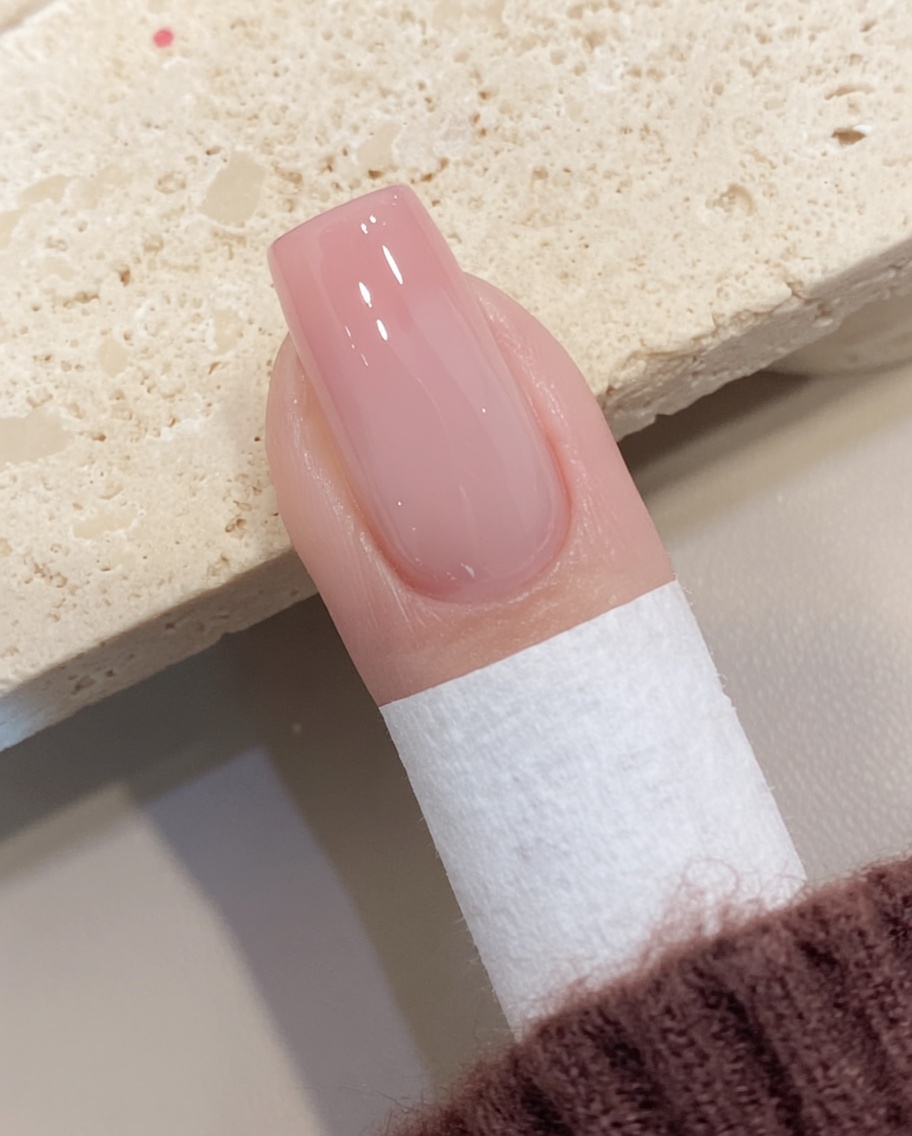 Una toallita sin pelusa eliminando el residuo pegajoso de una uña de gel curada.