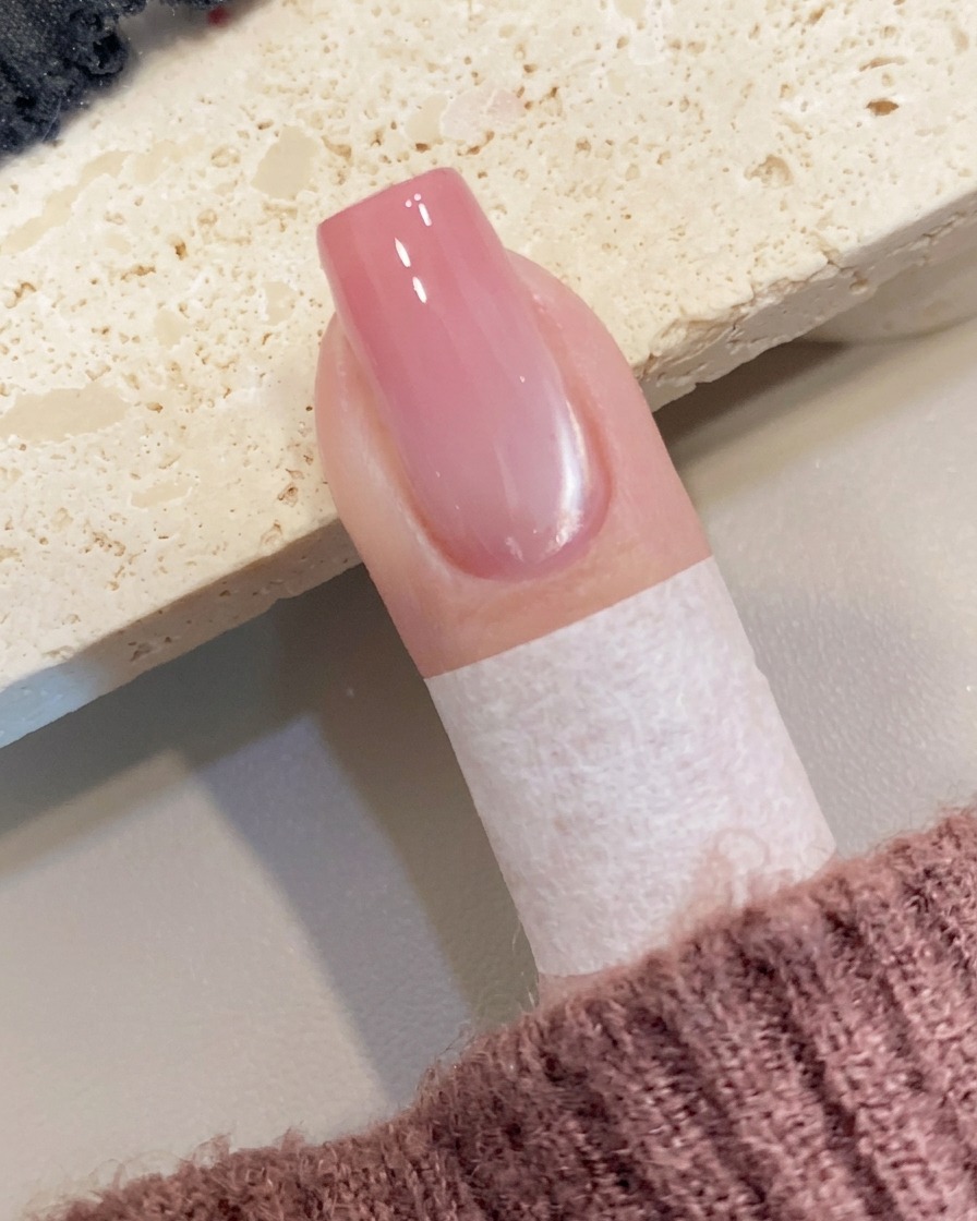 Una pequeña cantidad de gel color melocotón siendo colocado en el borde libre de la uña con un pincel.