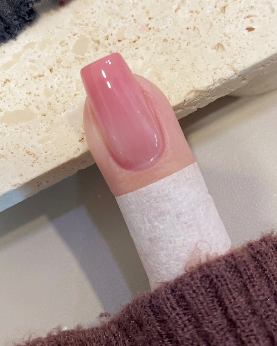 Un pincel aplicando una capa final de top coat transparente de alto brillo sobre una uña ombré melocotón.