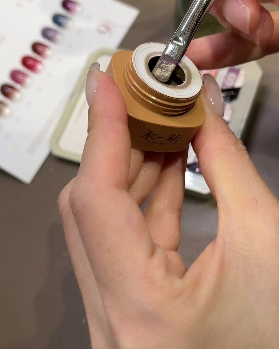 Un pincel aplicando gel cat-eye color melocotón beige sobre una punta de uña transparente.